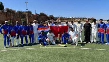 cricket in morocco players in blue and white kits pose together with indian and moroccan flags on an outdoor pitch
