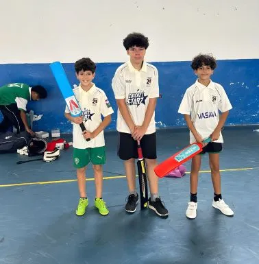 cricket in morocco three young players in white cricket shirts posing with blue, black and red bats inside a sports hall