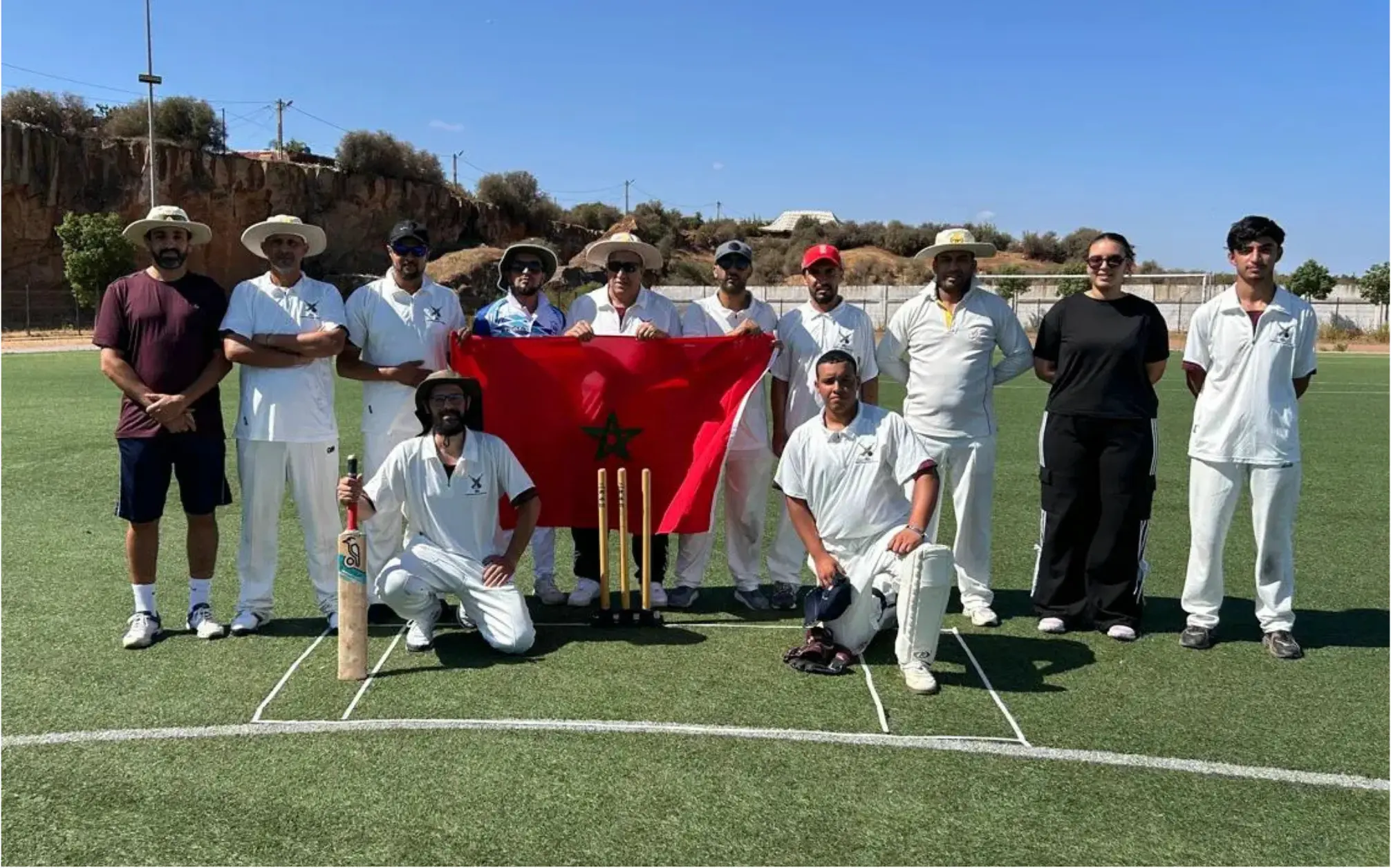 Cricket in Morocco: SJCU team posing on an outdoor pitch with the Moroccan flag, cricket bat and stumps.